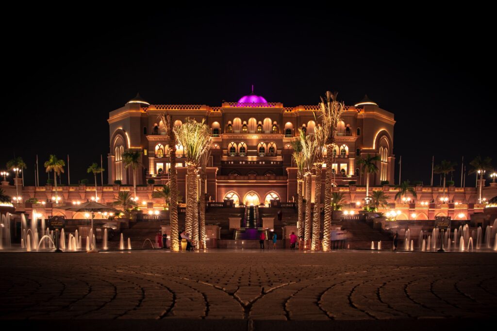 Wide shot of tropical trees and ground water fountains near Emirates Palace at night in Abu Dhabi